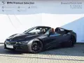 Ciemnoszary kabriolet BMW i8 z brązowym wnętrzem na tle białej ściany z logo BMW.