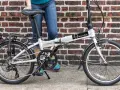 A person stands next to a silver Dahon Mariner folding commuting bike, ready for their next urban adventure.