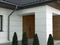 Nowoczesna elewacja z białym tynkiem i drewnianymi akcentami. Charakterystyczne boniowanie na elewacji podkreśla geometryczne kształty budynku.