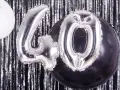 Srebrne balony z cyfrą 40 i biały balon na tle błyszczącej kurtyny. Idealne na zabawy na 40 urodziny!