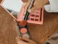 Hand hält Pinsel mit Tiger-Muster über Rouge und Lidschatten-Palette.
