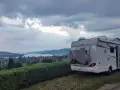 Kamper zaparkowany na kempingu w Czeskiej Szwajcarii, z widokiem na jezioro i wzgórza.