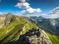 Widok na szlak prowadzący na Kasprowy Wierch. Zielone zbocza górskie, skaliste szczyty i błękitne niebo z chmurami.