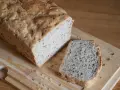 Chleb z siemienia lnianego, z jedną kromką obok, na desce do krojenia.