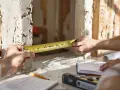 Mierzenie otworu pod drzwi 90 cm. Na stole leżą plany i poziomica.
