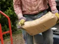 Mężczyzna w rękawicach niesie worek cementu. Zastanawia się, ile piasku na 25 kg cementu będzie potrzebne do budowy.