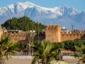 Marrakesz, gdzie leży, widać na tle ośnieżonych gór Atlas. Stare mury miasta i palmy tworzą malowniczy krajobraz.