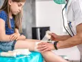 Lekarz opatruje ranę na nodze dziewczynki. Wczesne objawy tężca mogą być subtelne, dlatego ważne jest szybkie działanie.