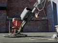 Robot do zacierania betonu pracuje na budowie. Robotnik w niebieskich spodniach kieruje maszyną, która wygładza świeżą posadzkę.