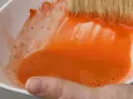 Maintenant, où jeter l'eau de rinçage des pinceaux ? Une main tient un bol blanc rempli d'eau orange trouble.
