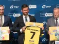 Trzech mężczyzn w garniturach prezentuje koszulkę z napisem "Galychanka" i numerem 7. Obok nich żółte pudełka z napisami "Poland Ukraine".