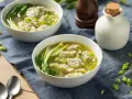 Dwie miseczki aromatycznej zupy won ton z zielonymi warzywami i posiekanym szczypiorkiem.