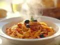 Un plato humeante de pasta con salsa de tomate, aceitunas negras y romero. ¡Perfecto para tus recetas de pasta!