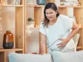 Frau mit schmerzverzerrtem Gesicht hält ihren Bauch, als ob sie Wehen erkennen würde.