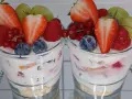 Zwei Gläser mit einem cremigen Dessert, garniert mit frischen Erdbeeren, Himbeeren, Blaubeeren, Johannisbeeren und Trauben. Ein köstliches Dessert im Glas.
