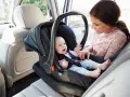 Uśmiechnięta mama patrzy na swojego **noworodka w foteliku samochodowym**, gotowego na podróż.