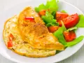Złocisty omlet francuski z kawałkami papryki, podany z sałatką z pomidorów i sałaty. Pyszne śniadanie.
