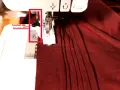 Levier de boutonnière sur machine à coudre, prêt pour réaliser une boutonnière parfaite sur un tissu bordeaux plissé.