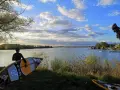 Ein junger Mann mit SUP-Board am Ufer des Alperstedter Sees. Der Himmel ist blau mit weißen Wolken, die Sonne scheint.