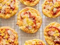 Mini pizze z serka wiejskiego, z kukurydzą i kawałkami mięsa, na metalowej kratce.