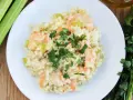 Kremowe risotto z krewetkami, ozdobione natką pietruszki, obok łodyg selera i oliwy.