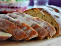 Pokrojony chleb z pomidorami, posypany mąką, leży na desce. W tle widać sałatkę.