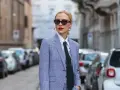 Mujer con traje a cuadros, camisa blanca y corbata negra, luciendo un impecable tomboy style. Gafas de sol y labios rojos completan su look.