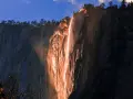 La luz del atardecer ilumina una cascada de fuego en un acantilado rocoso, creando un espectáculo natural.