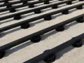 Rows of black synthetic lumber are elevated on black adjustable pedestals, creating a modern deck base on a concrete surface.