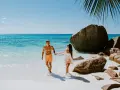 Para na Seszelach cieszy się idealną pogodą, spacerując po plaży z turkusową wodą i skałami.