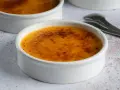 Dwa kremowe desery w białych naczyniach, z chrupiącą, karmelizowaną skórką. Crème brûlée czy crema catalana? Wybór należy do Ciebie!
