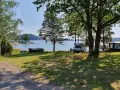 Solig dag vid vattnet på Kalvholmens camping. Husbilar och husvagnar står uppställda på gräsmattan nära sjön.