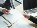 Przekazanie wypowiedzenia umowy na czas określony. Dwie dłonie, jedna w rękawie koszuli, druga w marynarce, trzymają białą kopertę.
