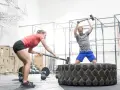 Kobieta i mężczyzna ćwiczą z młotami na oponie w siłowni CrossFit.