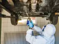 Mechanik w kombinezonie zabezpieczającym podwozie samochodu. Zastanawiasz się, ile kosztuje przegląd samochodu z gazem?