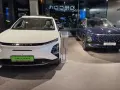 Dwa nowoczesne auta OMODA, białe i granatowe, prezentują się w salonie. To przyszłość motoryzacji, czyli auto hybrydowe.
