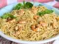 Un plato de espaguetis con gambas, adornado con hojas de albahaca fresca y perejil picado.