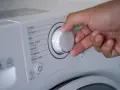 Mano ajustando el selector de la lavadora para saber como lavar un anorak. Se ven programas como "Cotton", "Mix", "Duvet".