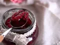 Słoik z domowym dżemem z czerwonej porzeczki, na łyżce widać apetyczne owoce.