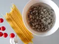 Składniki na pyszny makaron z małżami: spaghetti, pomidorki, czosnek i świeże małże w misce.