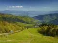 Widok na zielone **beskid mały szczyty** z kolejką linową i jeziorem w oddali.