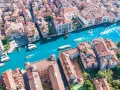 Vista aerea del **canale di Venezia** con gondole e vaporetti che navigano tra palazzi storici dai tetti rossi.