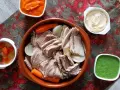 Un invitante bollito di carne, affettato e servito con carote, cipolle e tre salse: una rossa, una bianca e una verde.