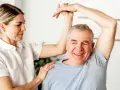 Physiotherapeutin unterstützt Mann bei Übungen zur Wiederherstellung der Beweglichkeit nach Schlaganfall. Verordnung Physiotherapie nach Schlaganfall wird umgesetzt.