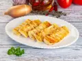 Grillowany ser halloumi na białym talerzu, z dodatkami jak czosnek, cebula i pomidory w tle.