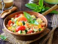 Un piatto colorato con couscous, pomodori, zucchine e peperoni, perfetto per una ricetta cous cous originale e fresca.