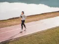 Une femme souriante profite d'une marche rapide sur une piste de course, au bord d'un lac paisible.