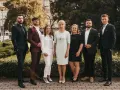 Grupa sześciu profesjonalistów w eleganckich strojach stoi przed budynkiem i zielenią.