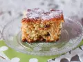 Kawałek klasycznego ciasta marchewkowego, posypanego cukrem pudrem, na szklanym talerzyku.