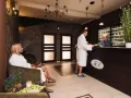Recepcja w hotelu dla dorosłych. Kobieta w szlafroku siedzi, mężczyzna rozmawia z pracownikiem.
